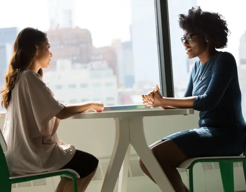 Two colleagues talking at a table by an office window